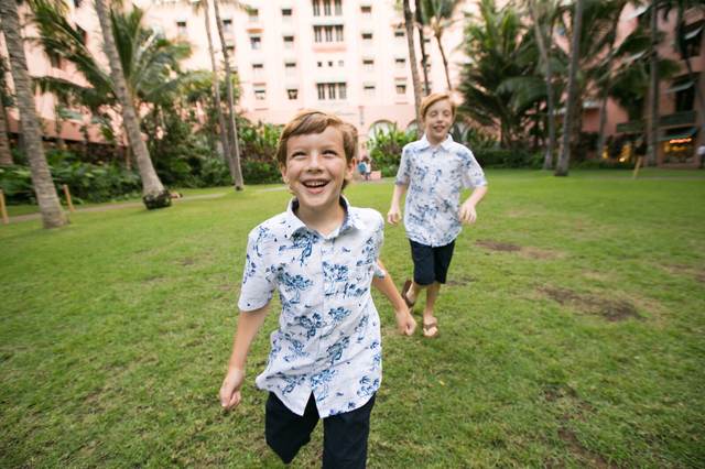 Two brothers running and laughing across a lawn near a pink hotel