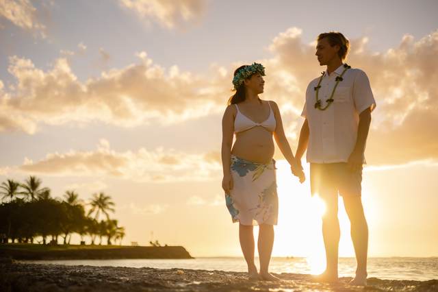 Pregnant couple holding hands on the beach at sunset