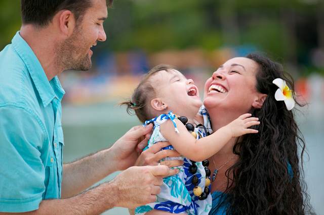 Father and mother laughing while holding their toddler