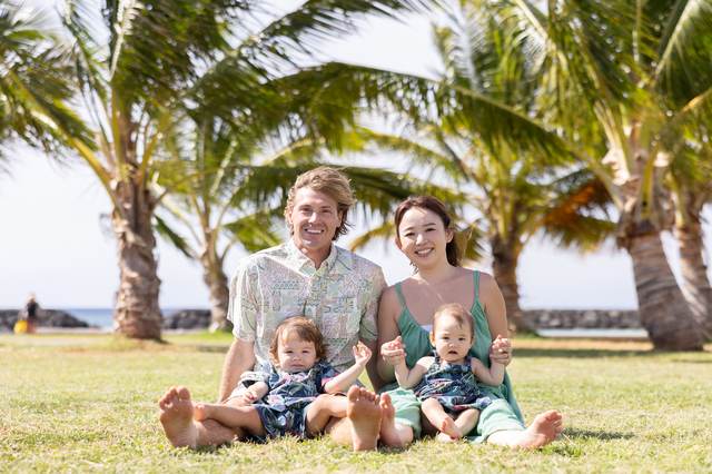 Parents sitting on the grass with two children under palm trees
