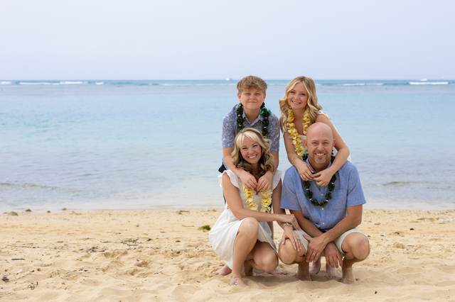 Family of four kneeling together on the sand at golden hour