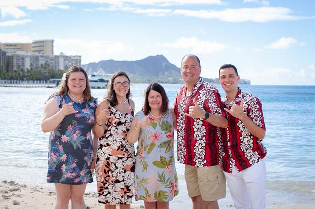 Group of five in colorful outfits posing on the beach with Diamond Head in the background