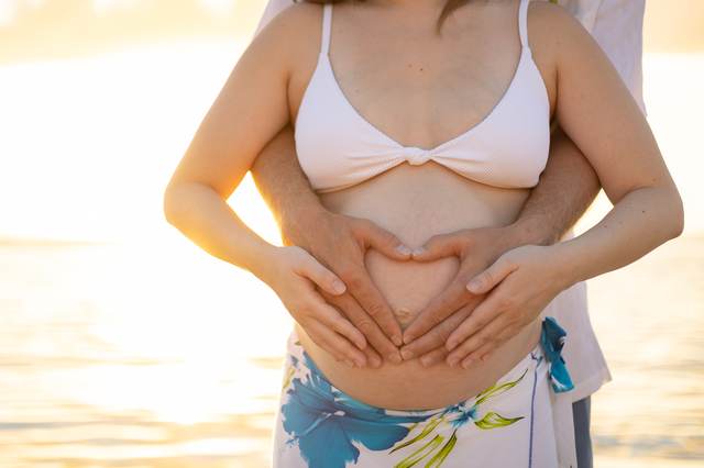 Close-up of a pregnant belly with hands forming a heart shape