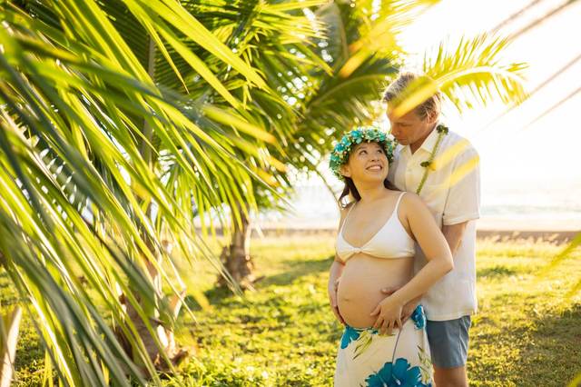 Pregnant couple embracing under palm trees wearing a flower crown