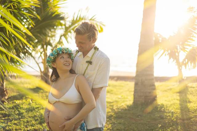 Pregnant couple embracing at sunset wearing flower leis