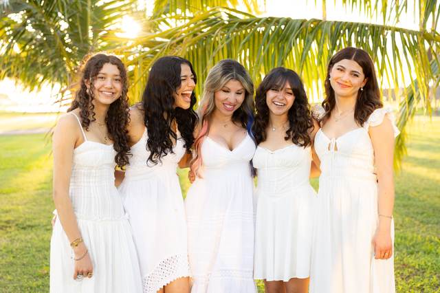 Mother and four daughters laughing under a palm tree at golden hour