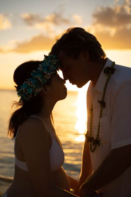 Close-up of a couple kissing at sunset wearing flower leis
